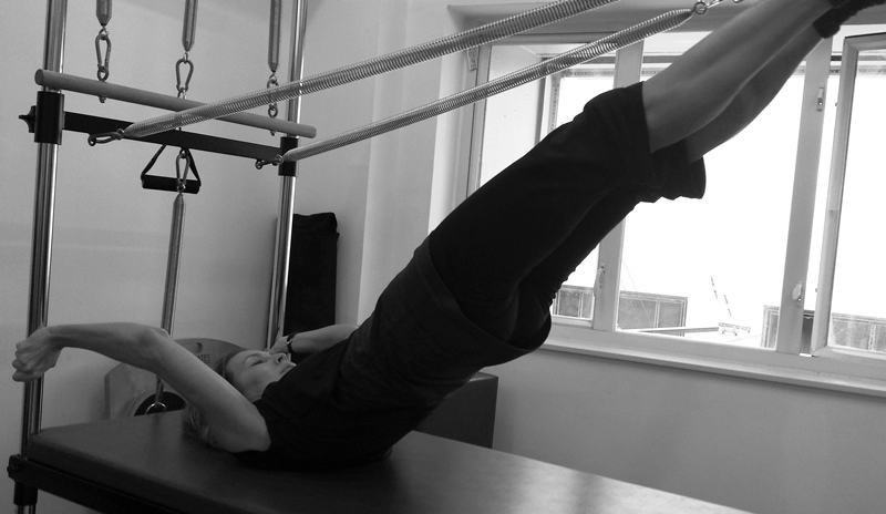 Pilates Instructor demonstrating advanced exercise on Cadillac